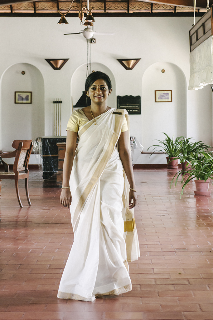 A beautiful young Indian woman dressed in a traditional cream with gold trim Keralan sari walks gracefully across the terra cotta tiled lobby of the CGH Earth hotel Brunton Boatyard in Fort Kochi, Kerala.