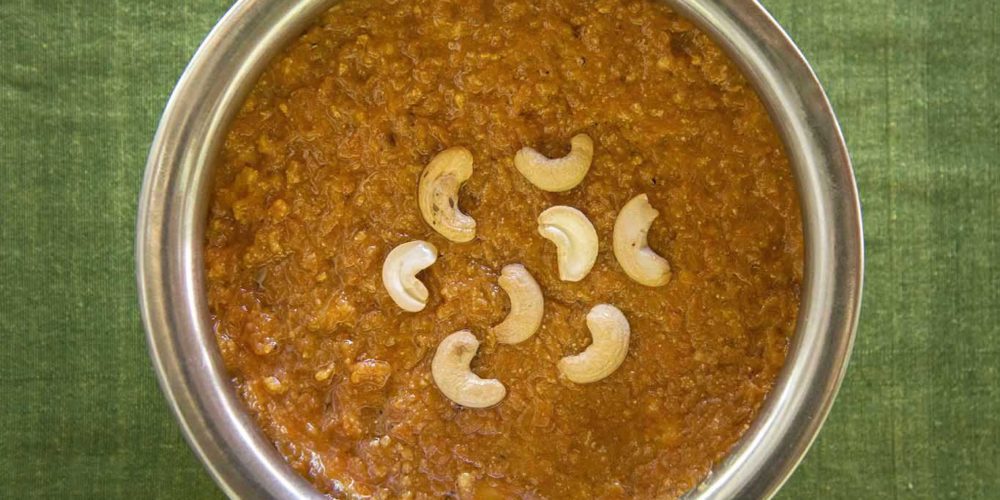 Bright orange carrot halwa in a round serving dish topped with halved cashew nuts. As prepared at The Bangala, Karaikudi.