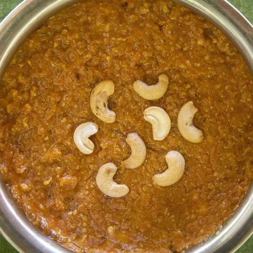 Bright orange carrot halwa in a round serving dish topped with halved cashew nuts. As prepared at The Bangala, Karaikudi.