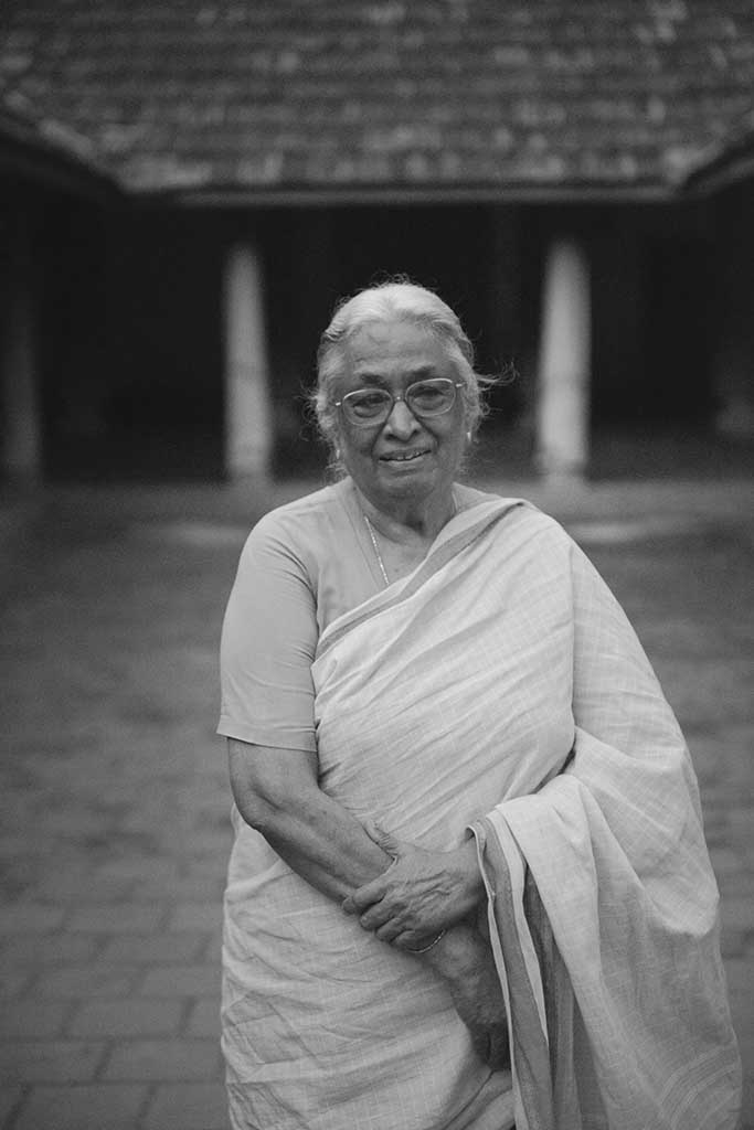 A black and white portrait of Mrs. Meenakshi Meyyappan, proprietor of The Bangala Hotel, in the courtyard of her Karaikudi home.