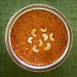 Bright orange carrot halwa in a round serving dish topped with halved cashew nuts. As prepared at The Bangala, Karaikudi.