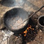 Shelled whole cashews roast over a fire positioned on the ground.