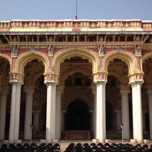 The massive white columns of Nayakar Mahal Palace tower above the central courtyard, where black folding chairs are set up for a performance.