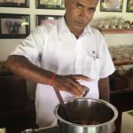 Raman, pastry chef at The Bangala Hotel in Karaikudi looks up at the camera as he adds a tasty ingredient to a large pot.