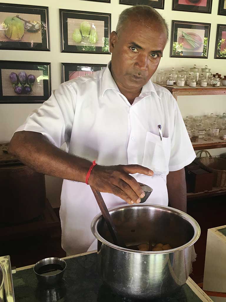 Raman, pastry chef at The Bangala Hotel in Karaikudi looks up at the camera as he adds a tasty ingredient to a large pot.