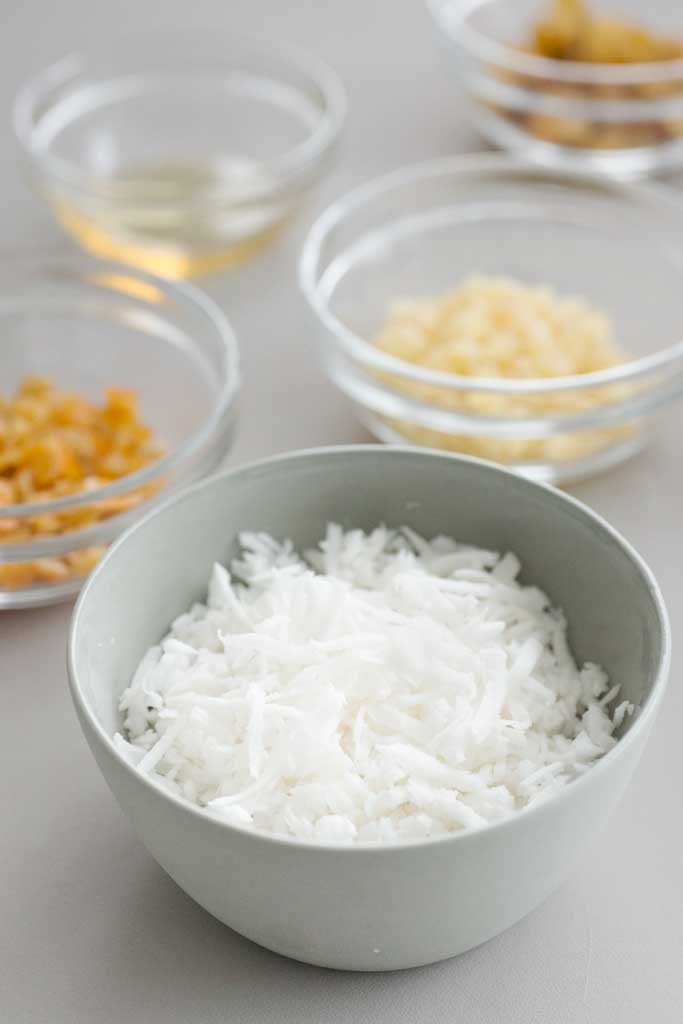 Coconut, candied ginger and citrus peel sit in small glass bowls.