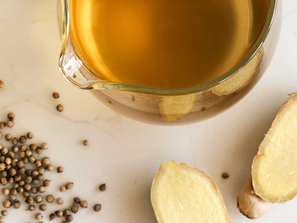 Sukku Coffee sits in a glass pot. Ginger and whole coriander seeds garnish.