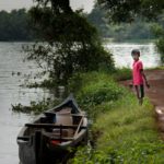 A boy waits by transport, a canoe along the Kerala Backwaters.