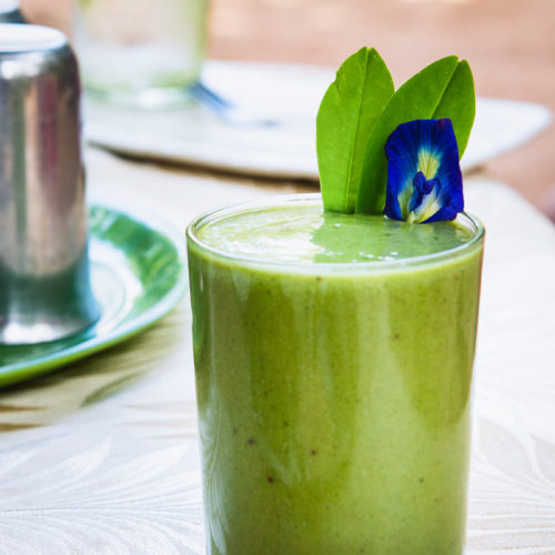 A green and minty smoothie with a purple flower garnish