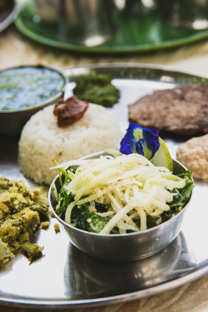 Small portions of colourful South Indian food sit in a circle on a white plate.