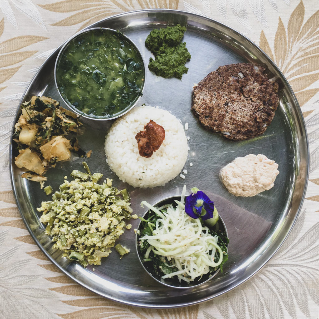 Small portions of colourful South Indian food sit in a circle on a white plate.