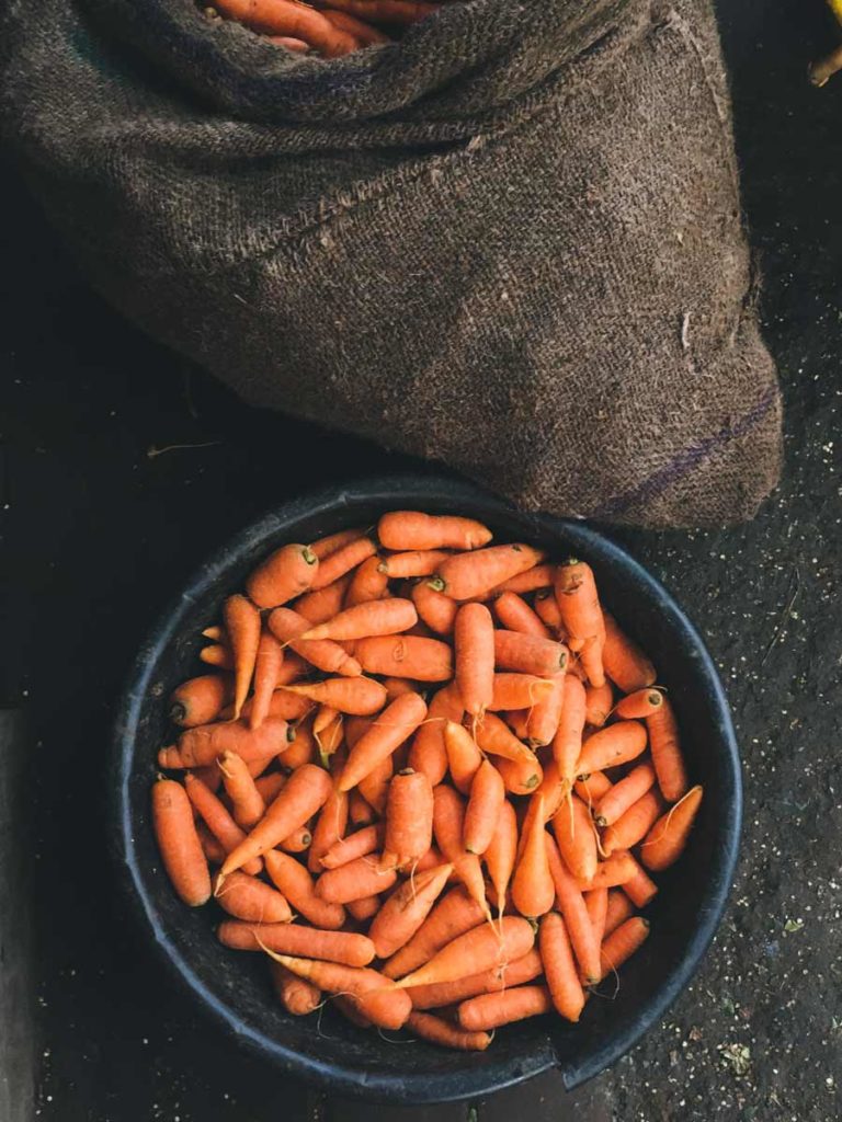 Small orange carrots in a bowl beside a sac.