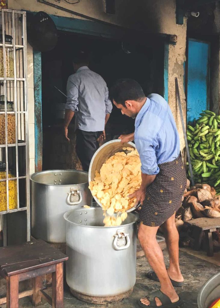 Man pouring sliced bananas into large steel container.