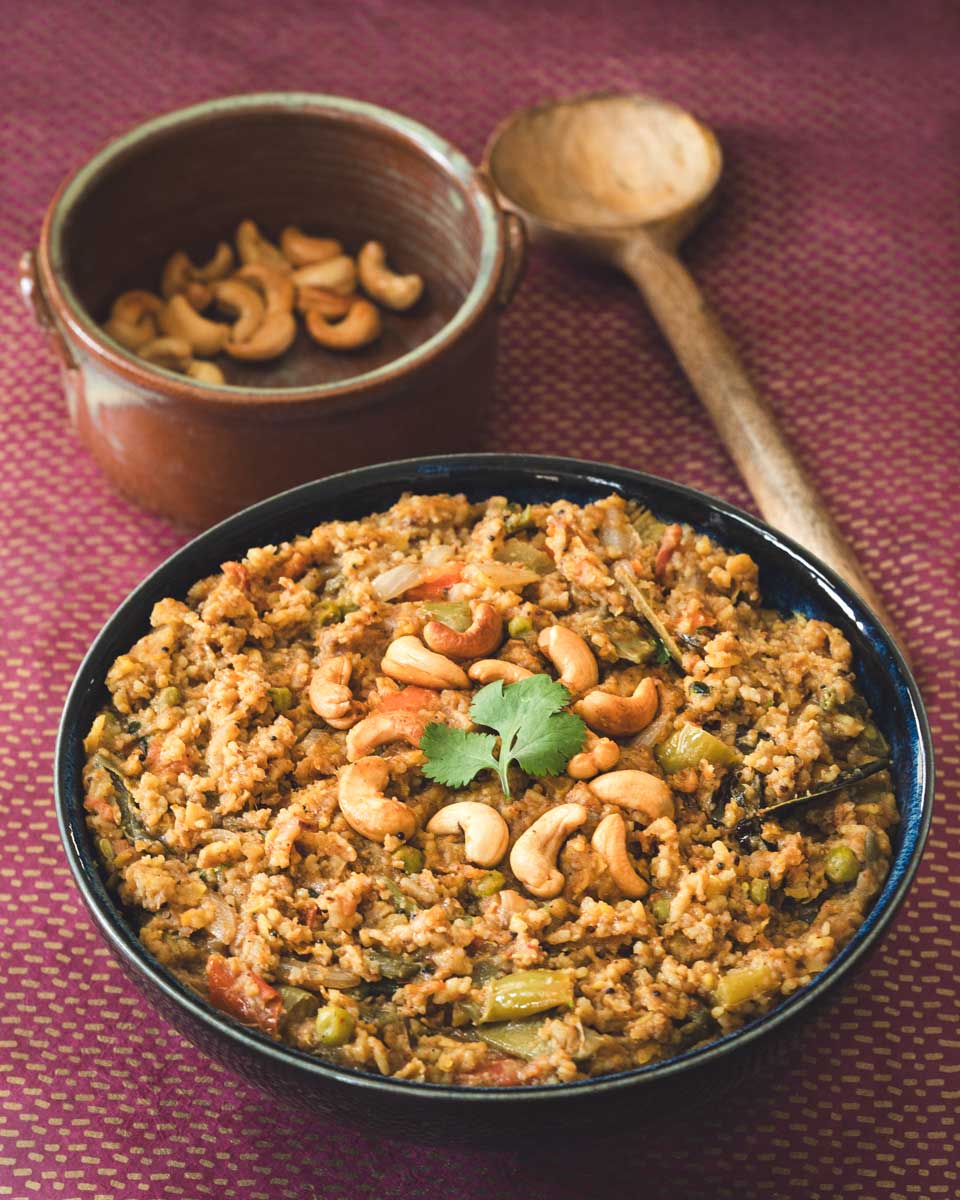 a bowl full of a rice and lentil dish with a bowl of cashews in the back